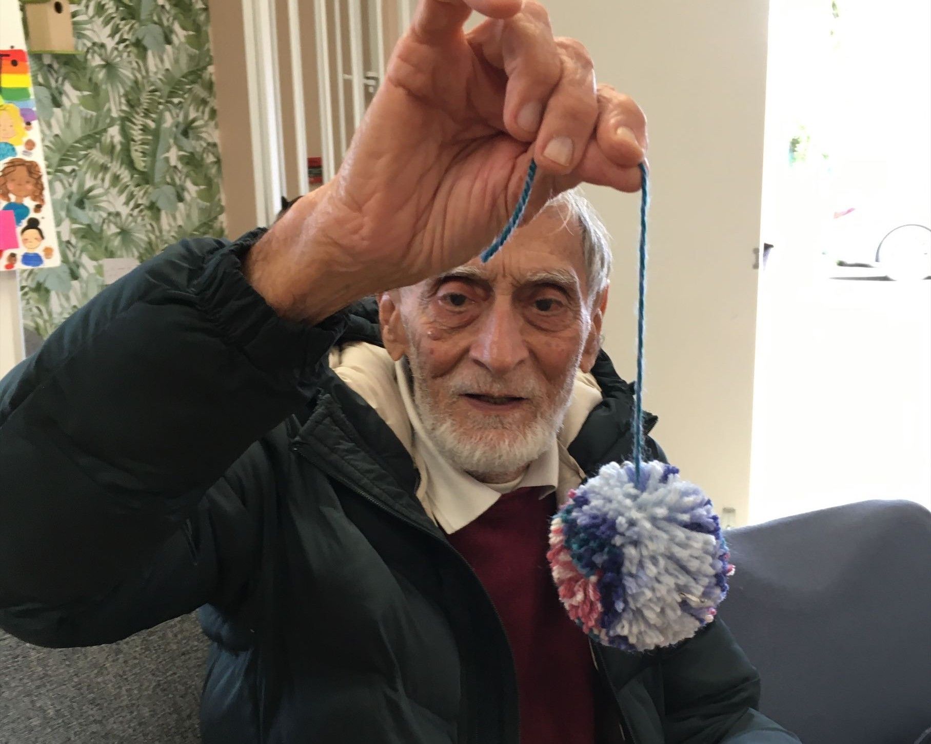 An elderly man is holding a pom pom in his hand while sitting on a couch.