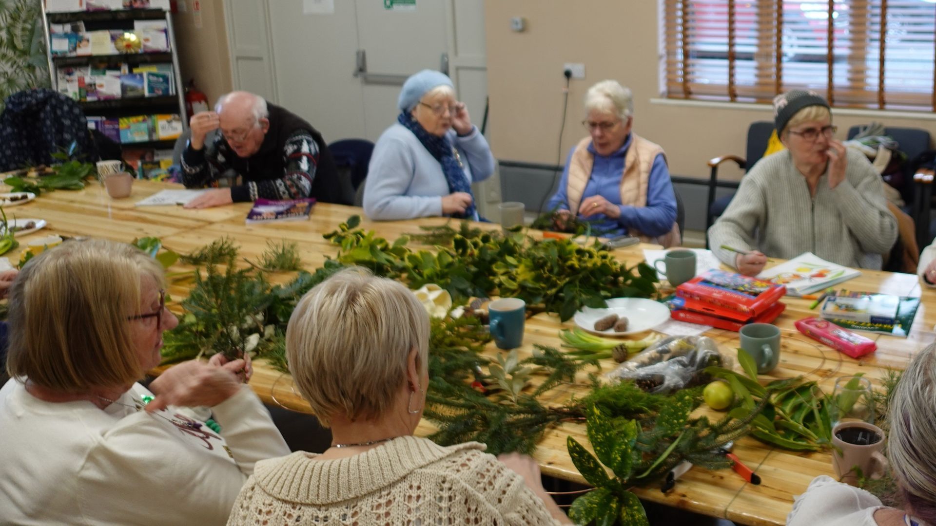 A group of people are sitting around a table making a wreath.