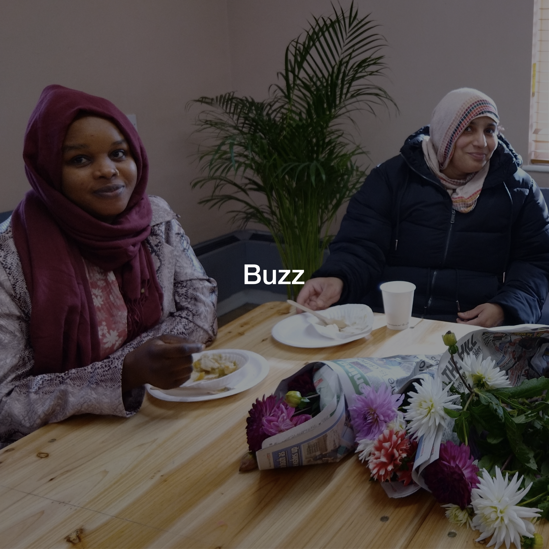 Two women sit at a table with plates of food and the word buzz on the bottom