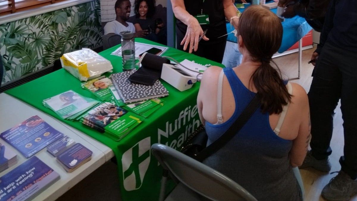 A woman is sitting at a table with a green table cloth that says nuffield health