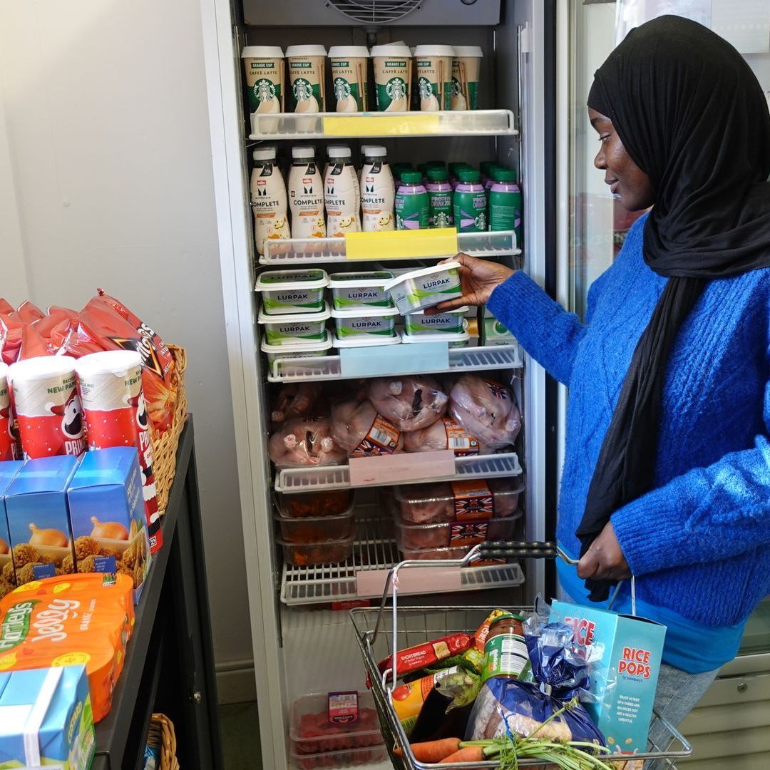 Aoman in a headscarf takes food from a fridge to put in a shopping basket