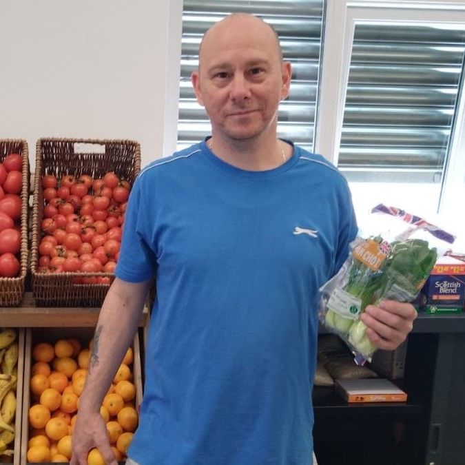 A man in a blue shirt is holding a bag of vegetables