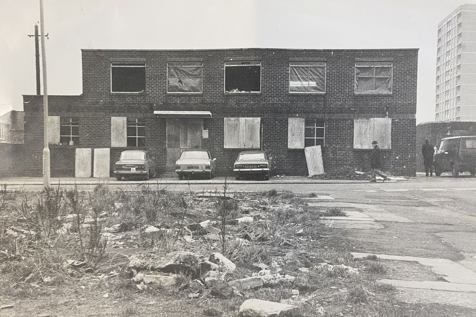 A black and white photo of a brick building with cars parked in front of it.
