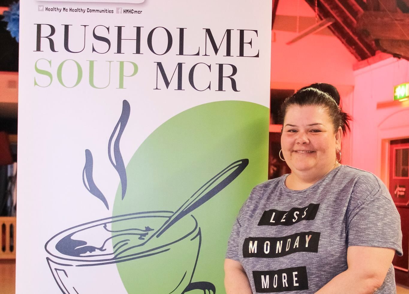 A woman stands in front of a sign that says rushholme soup mcr