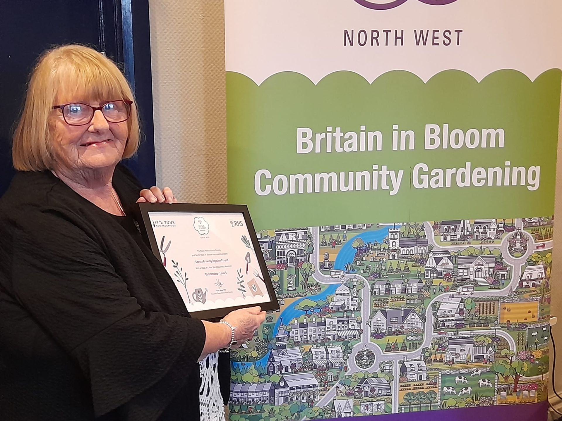 Pat Lamb holds the award in front of a banner for Britain in Bloom 'Community Gardening'