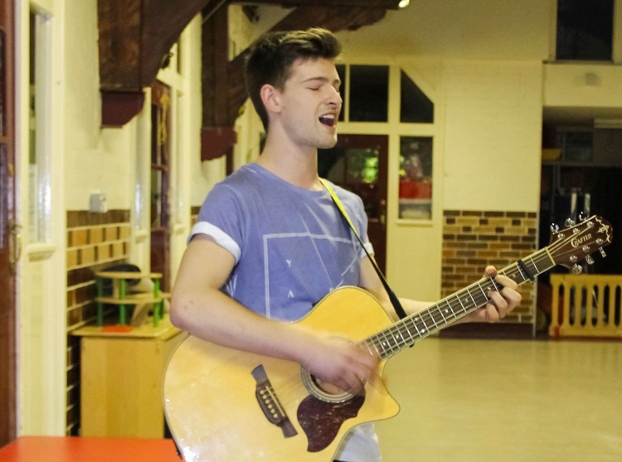 A young man is singing while holding a guitar
