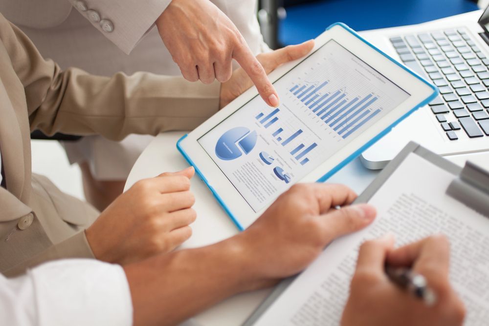 Personas revisando datos financieros en una tableta. Una persona señala un gráfico de barras.