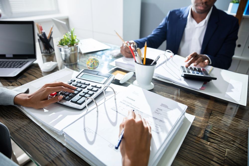 Dos personas trabajando en un escritorio con calculadoras y papeleo.