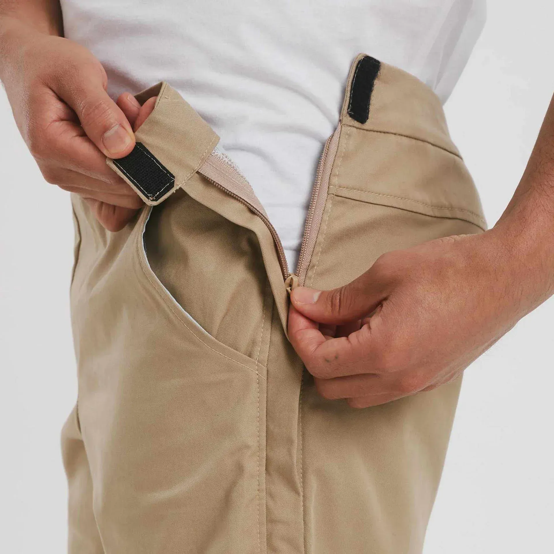 Man adjusting the zipper of khaki pants, with Velcro closures at the waistband.