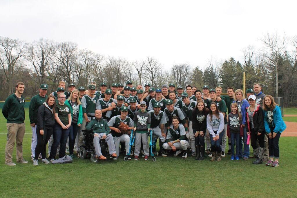 Group of people in MSU green and gray baseball uniforms on a baseball field.