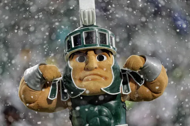 Spartan mascot flexing in the snow, wearing helmet and green armor.