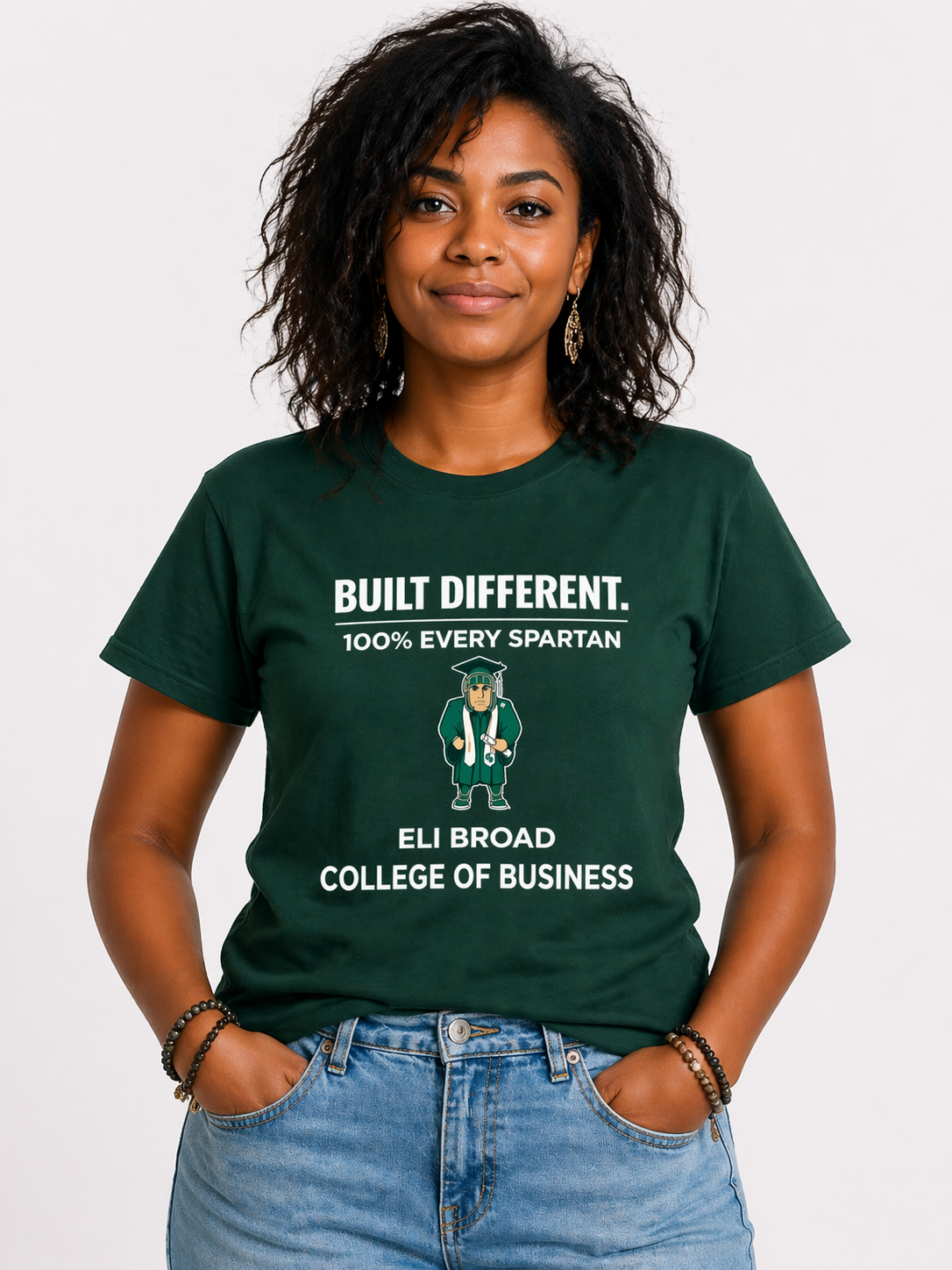 Woman in green “Built Different” T-shirt and jeans standing against a white background.