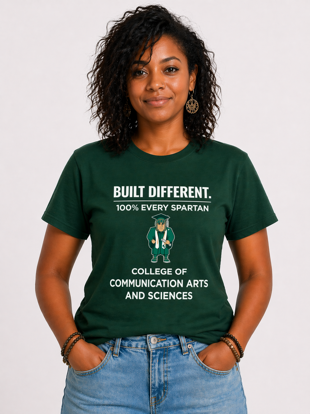 Person standing against a white background, wearing a green “Built Different” college t-shirt and jeans.