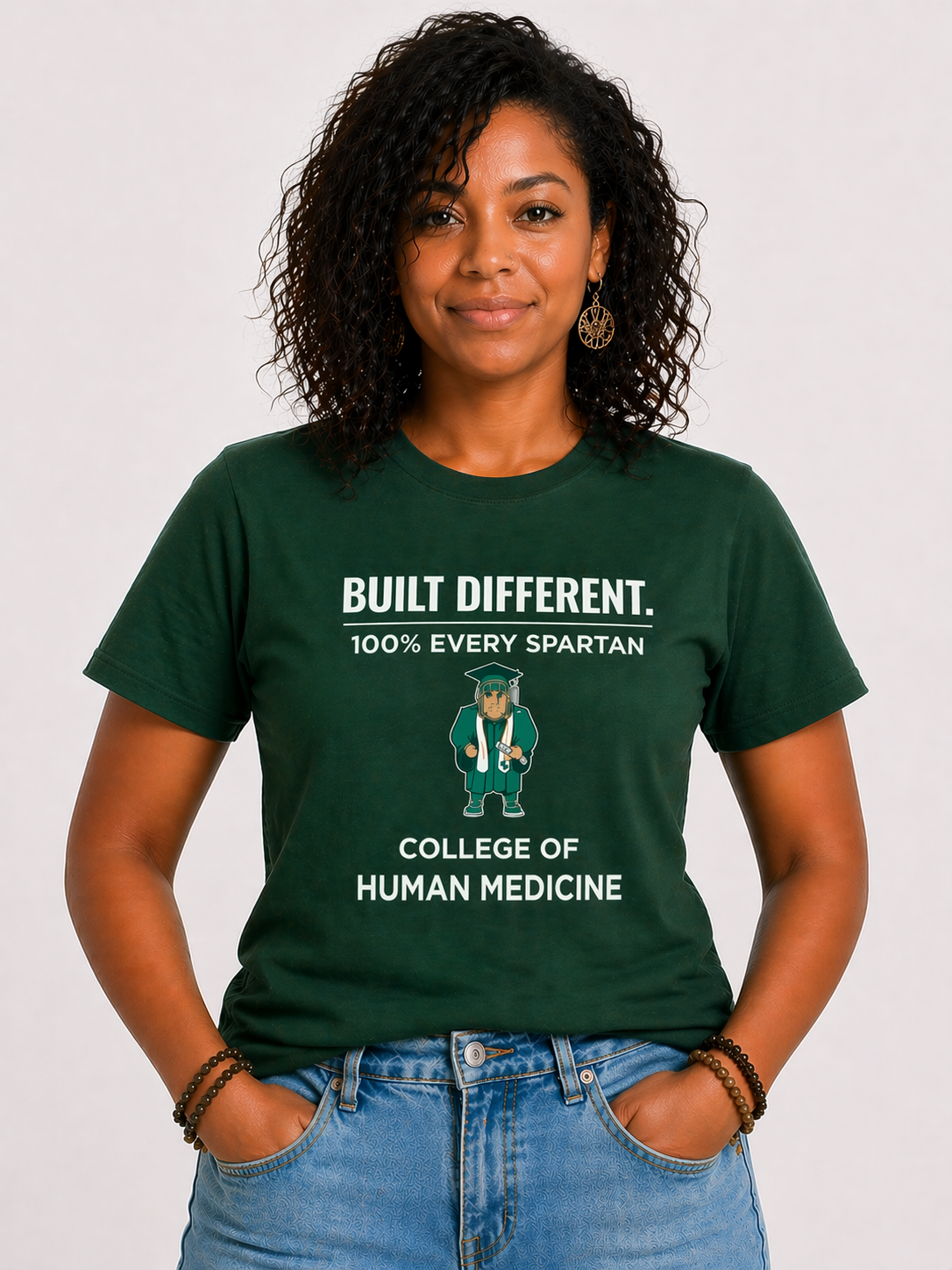 Woman in green “Built Different” T-shirt and jeans standing against a white background