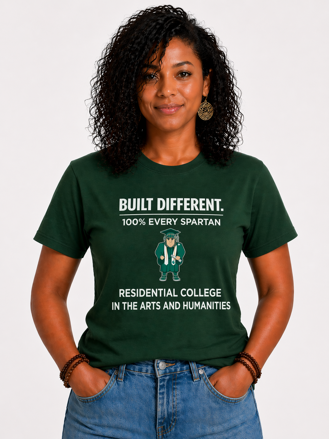 Person in a green graphic T-shirt and jeans, standing with hands in pockets against a plain background.