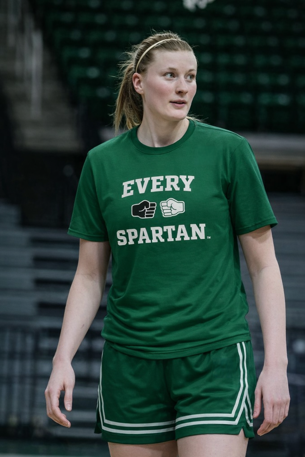 Woman in green Spartan gear stands on a basketball court, looking to her right.