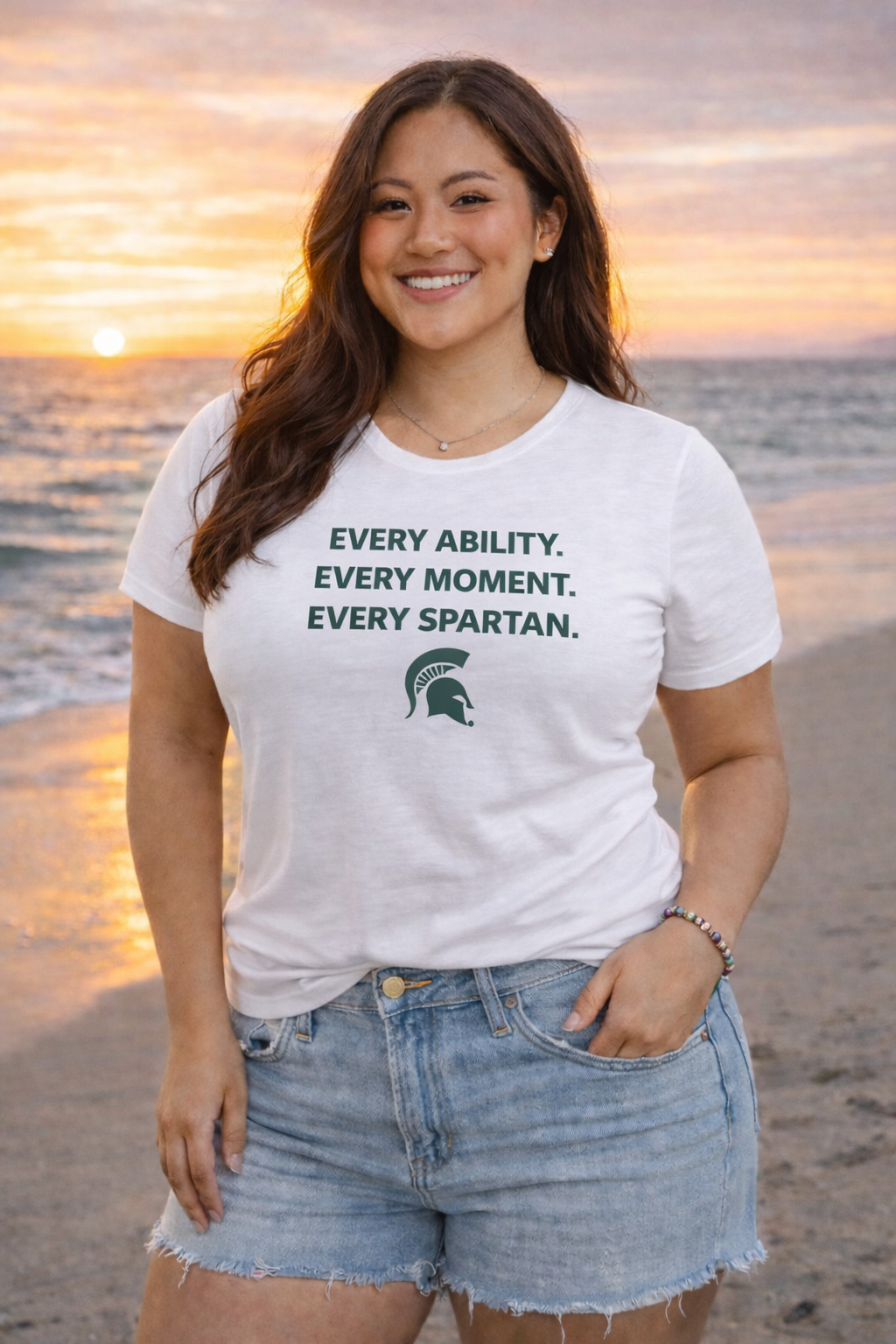 Woman on beach wearing a white t-shirt and denim shorts, smiling at sunset.