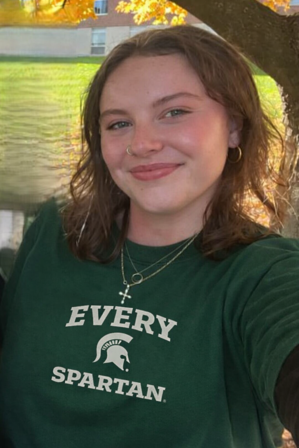 A smiling person wearing a green Michigan State University 
