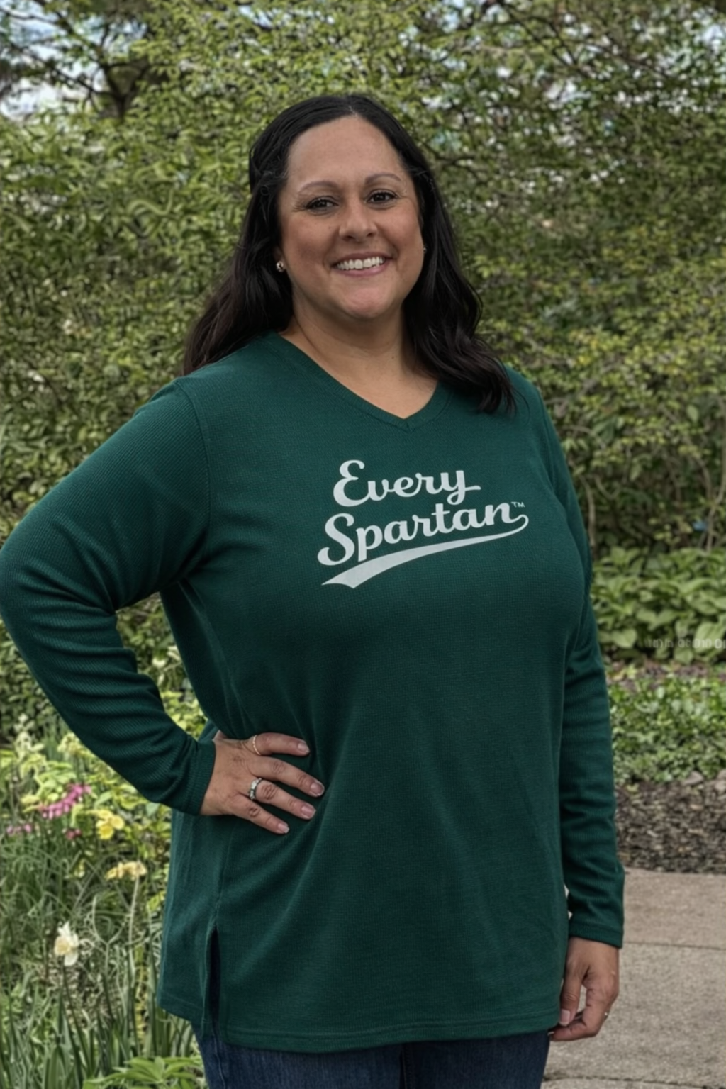 A person smiling while wearing a dark green long-sleeve shirt that says 