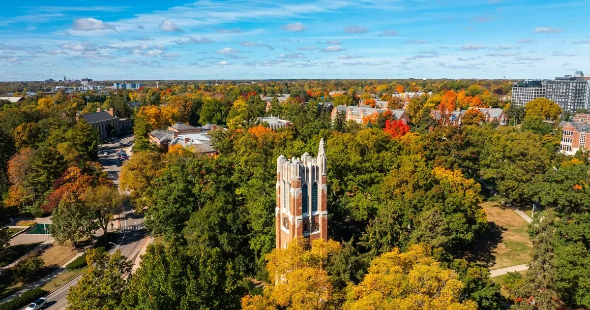 Aerial view of brick bell tower surrounded by fall foliage, under a blue sky.