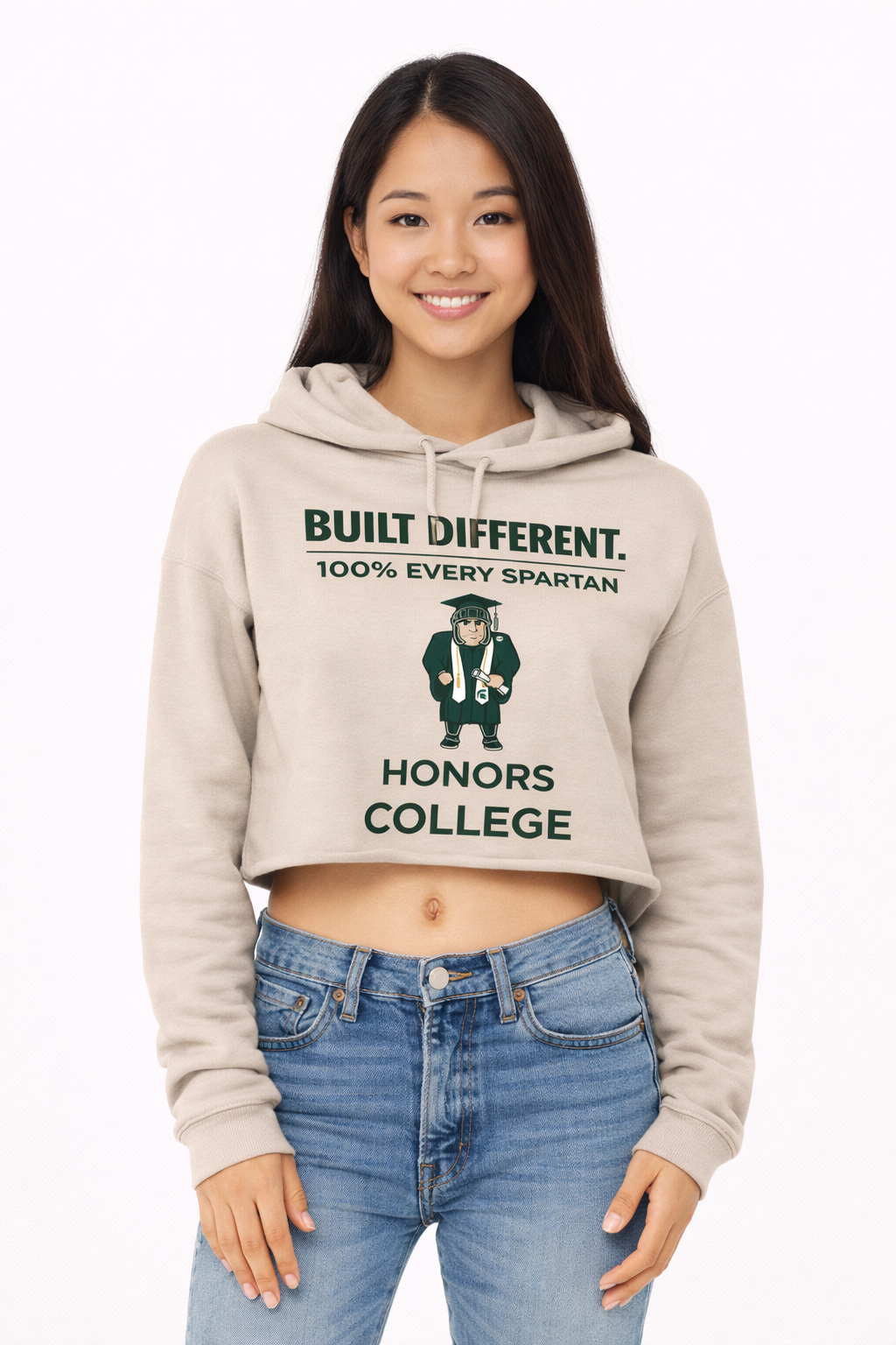 A woman wearing a tan cropped hoodie featuring a Spartan mascot graphic and the text 