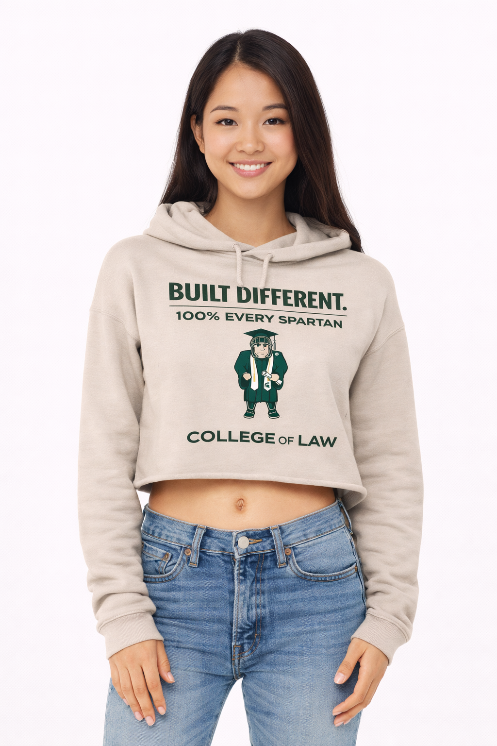 A smiling person wearing a beige, long-sleeved cropped hoodie featuring a green 