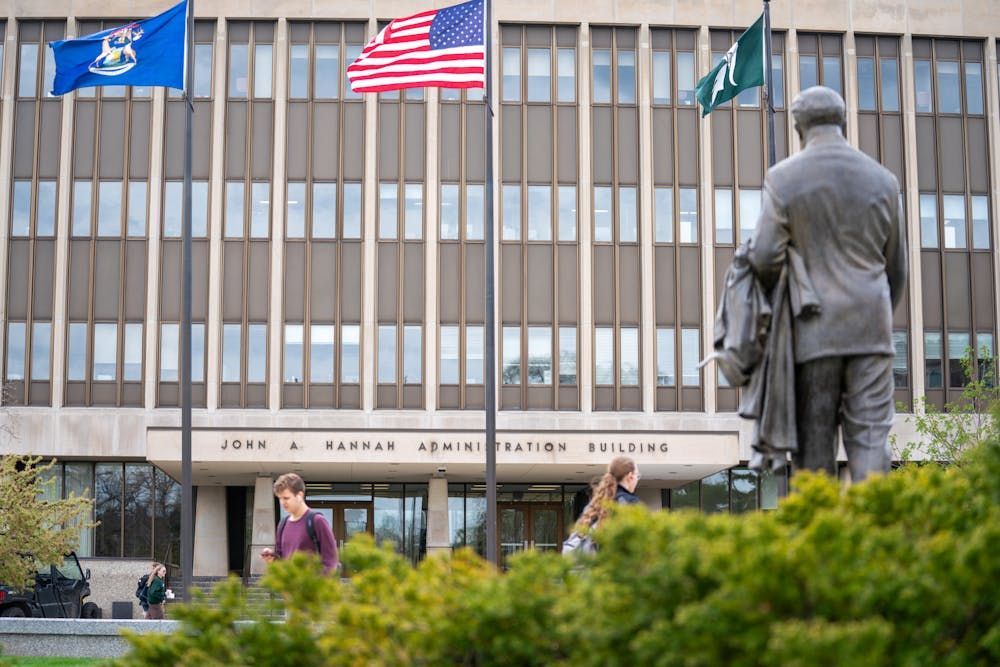 John Hannah Administration Building with flags, statue, and people walking outside.
