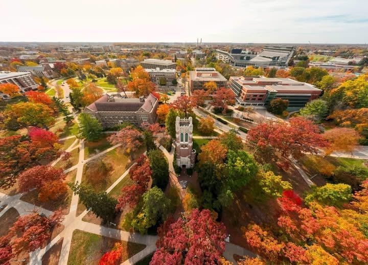 Aerial view of university campus with fall foliage in vibrant colors. Buildings and a bell tower are visible.
