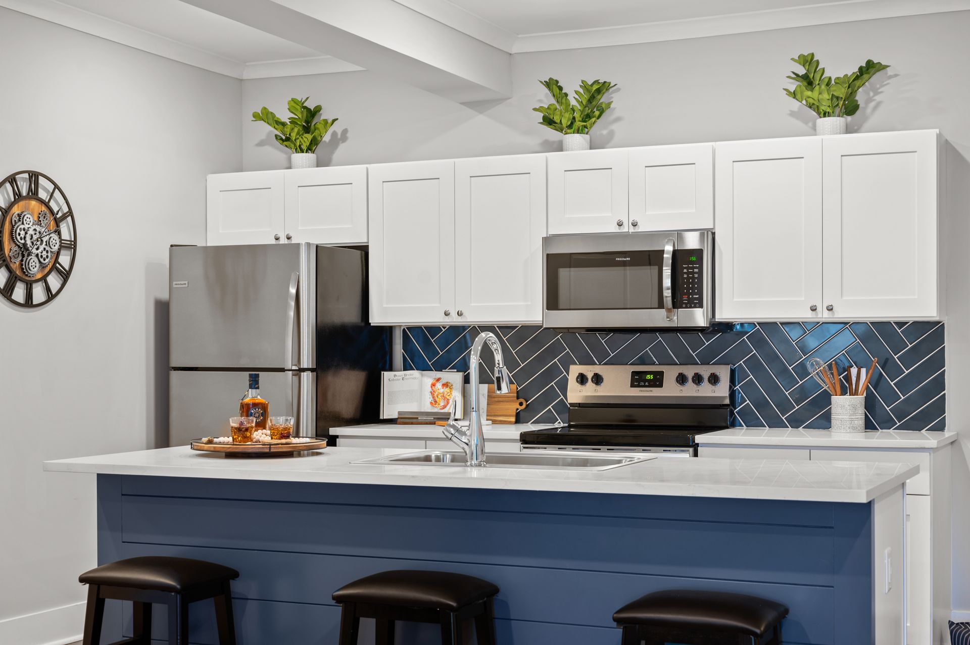 The apartment kitchen with a blue island, white cabinets, stainless steel appliances, and a clock on the wall .