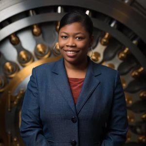 A woman in a blue suit is smiling in front of a vault door