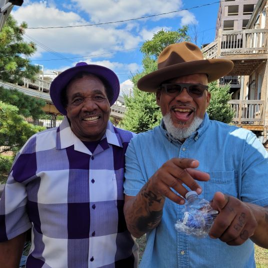 Two men are posing for a picture and one is wearing a purple hat