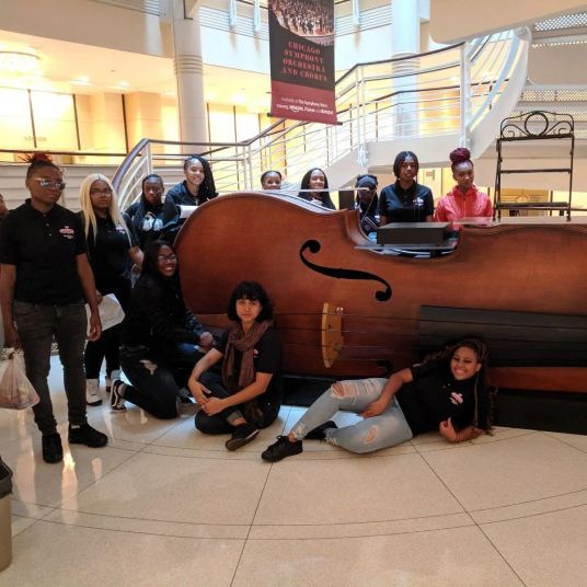 A group of people posing in front of a large violin