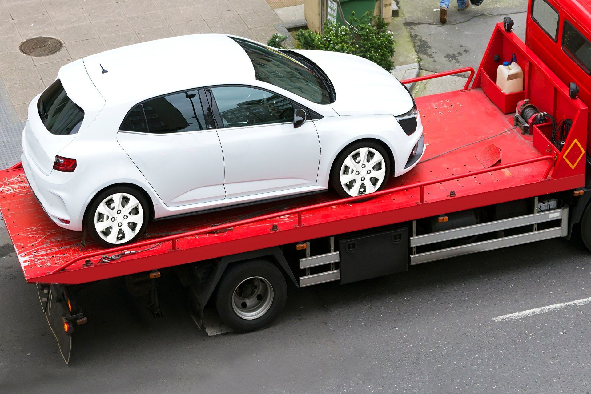 White car on a red tow truck, on a street.