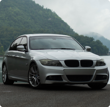 Silver BMW sedan parked on a paved area, with a mountain and lake in the background.