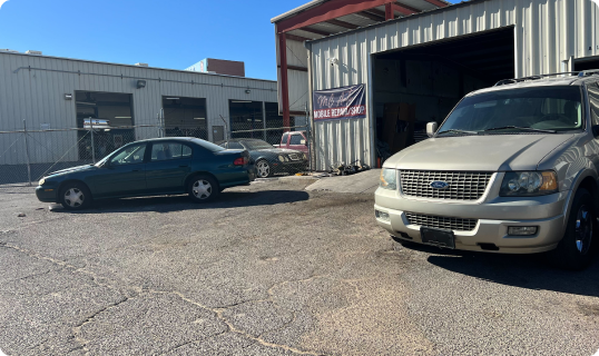 An auto repair shop with a green sedan and a beige SUV parked outside.