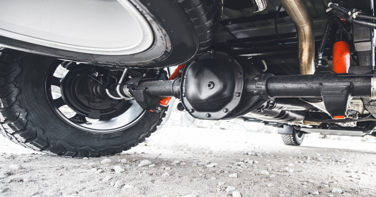 Undercarriage of a black truck showing the rear axle, tire, suspension, and exhaust components.