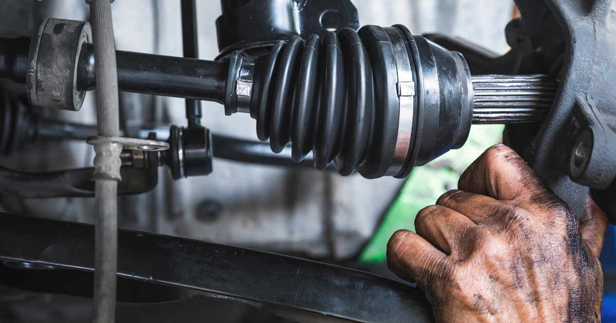 Mechanic's hands working on car's axle. Close-up shows dirty hands, black rubber boot, and metal parts.