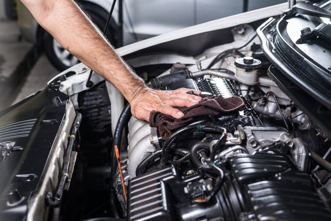 Mechanic's hand wiping down a car engine in a garage.
