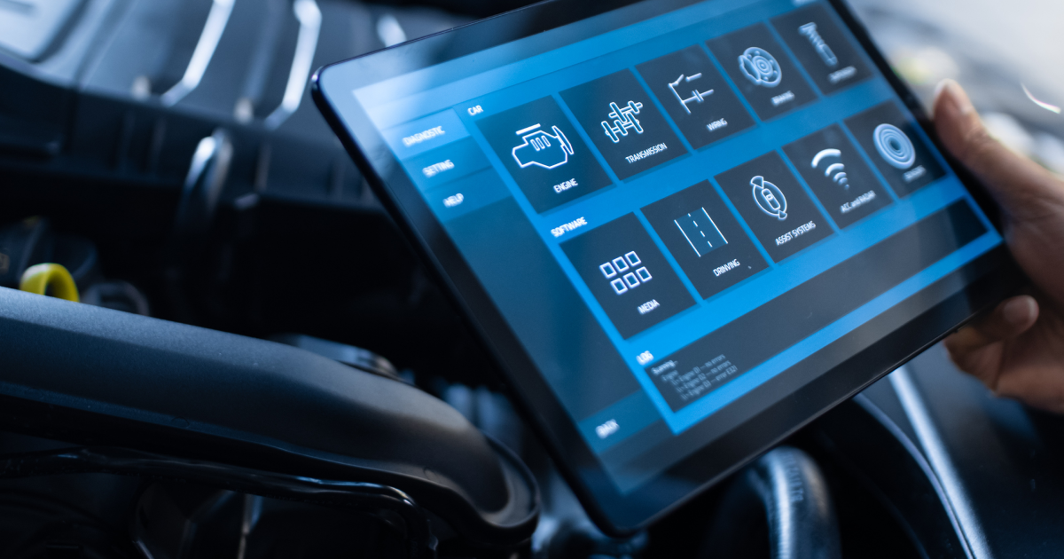 Mechanic using a tablet to diagnose a car engine with a blue-lit interface.