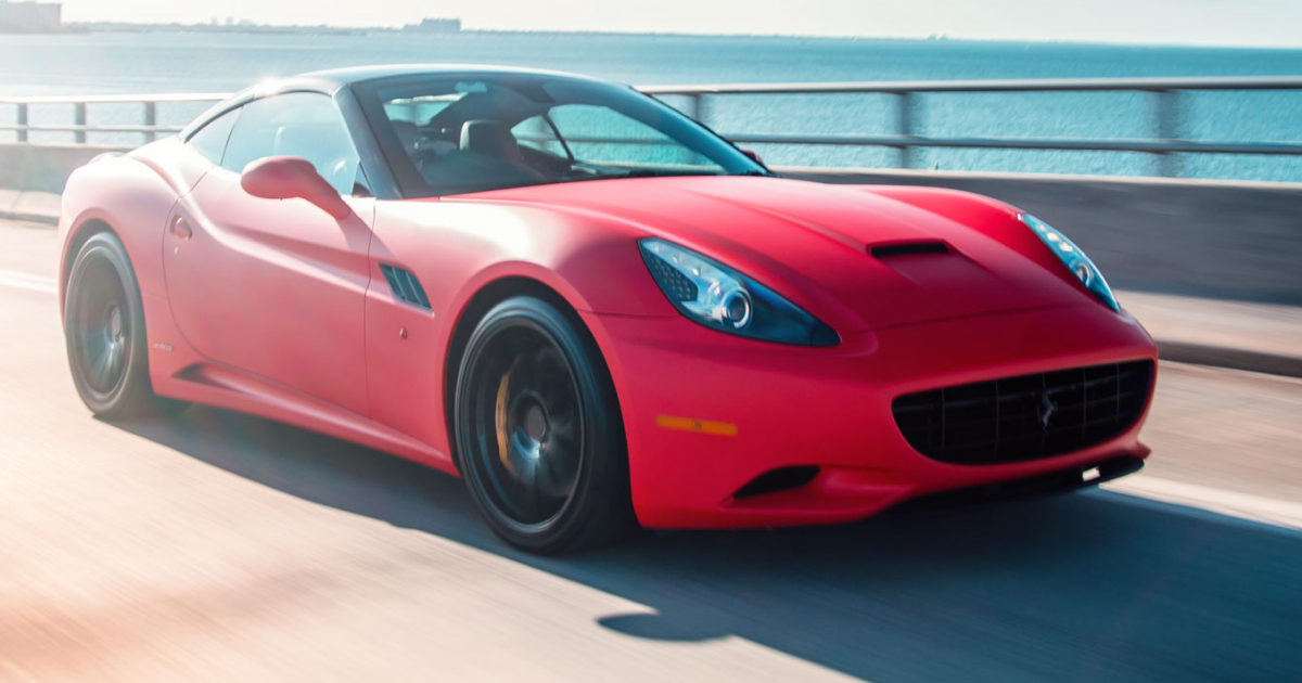 Red Ferrari California sports car speeding on a bridge, against a bright sky.