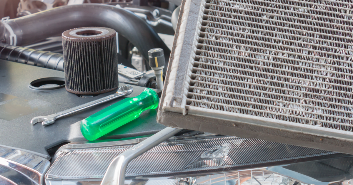Car parts, including a dirty filter, wrench, and screwdriver, on a car's hood.