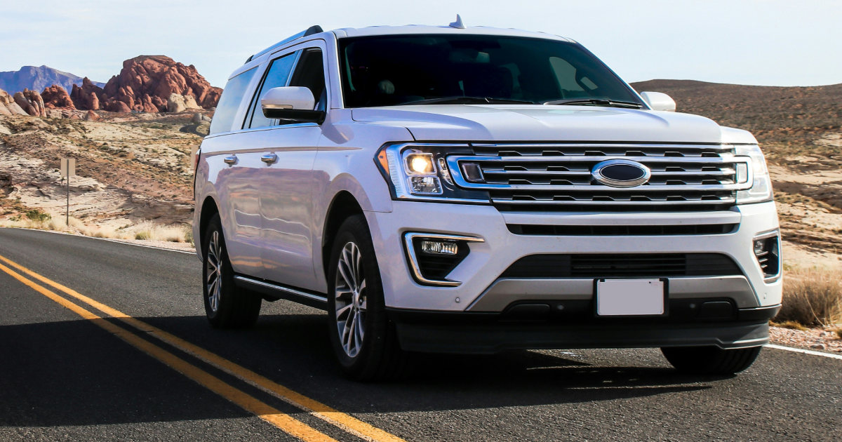 White Ford Expedition SUV on a desert road with rock formations in the background.