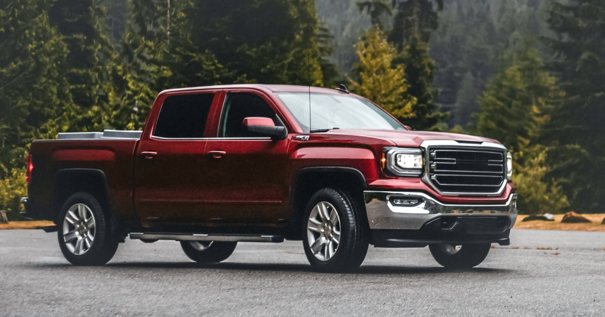 Red GMC Sierra pickup truck parked on a wet road in front of a forest.