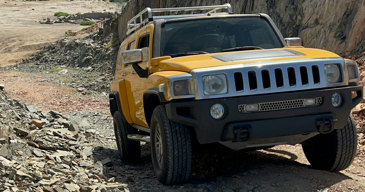 Yellow Hummer SUV off-roading on a rocky dirt path, angled up, sunny day.
