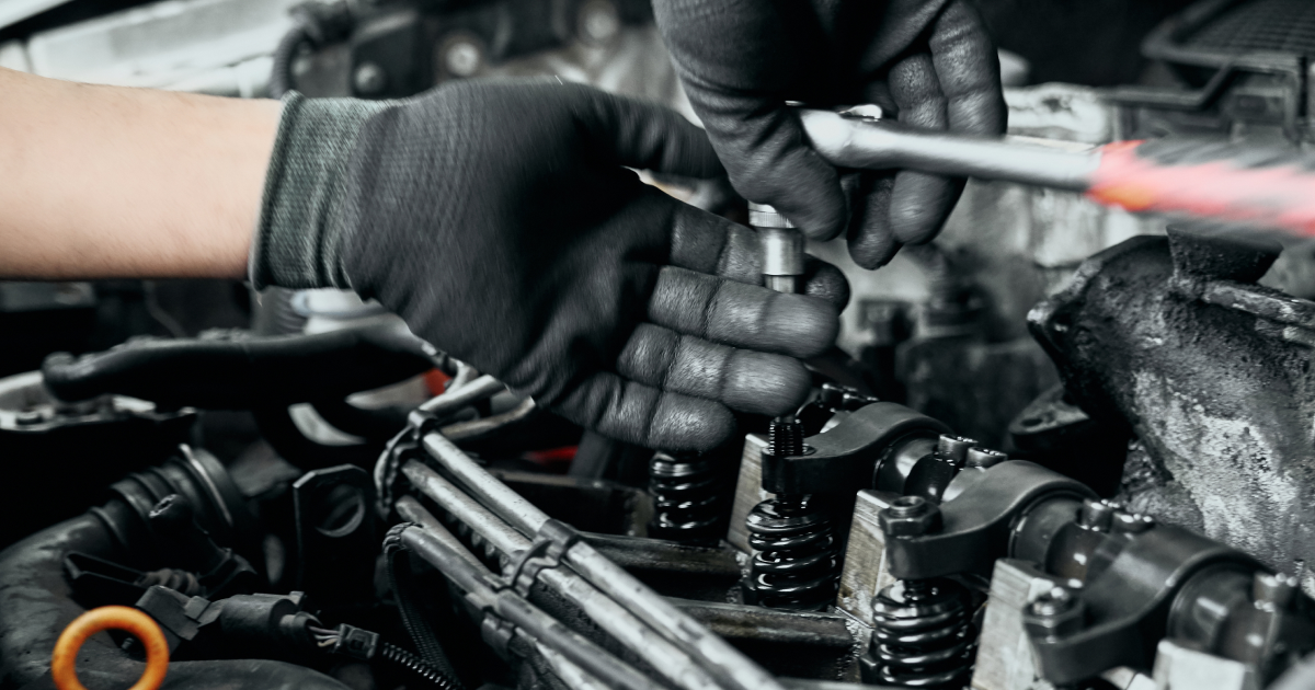 A mechanic's gloved hands work on a car engine, using a wrench to loosen a bolt.