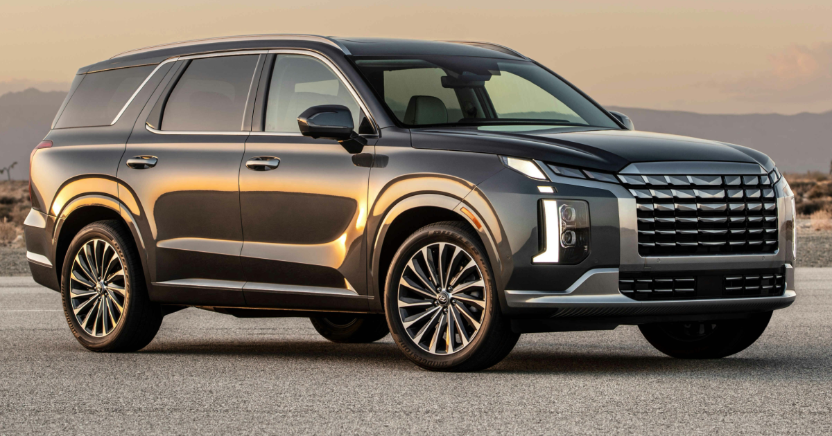 Dark gray Hyundai Palisade SUV on asphalt, mountains in the background.