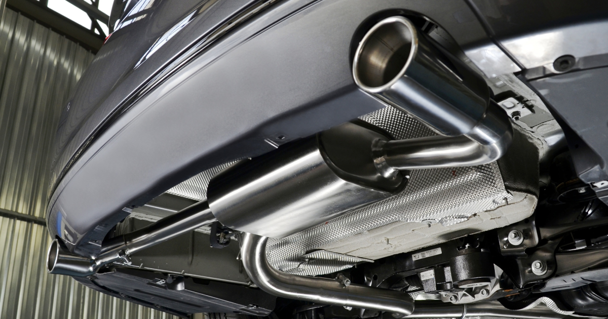 Underside view of a silver car showing exhaust system with muffler and tailpipe, in a garage.