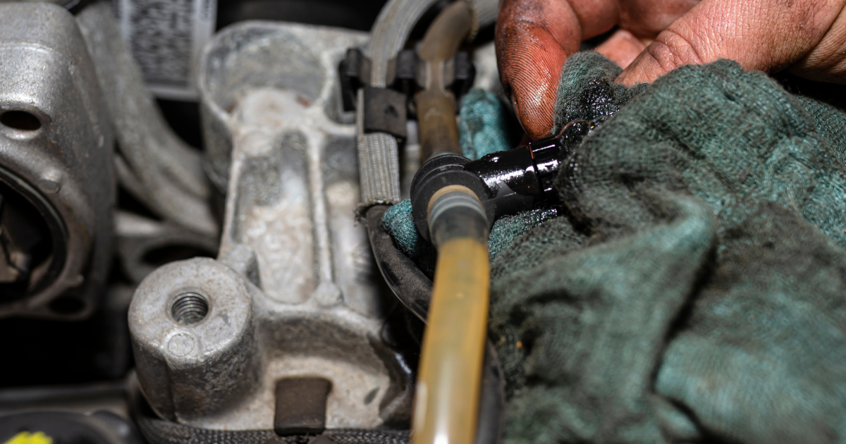 Person wiping oil from a car engine fitting with a rag.