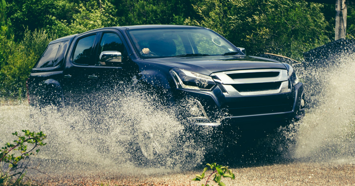 Dark blue pickup truck fording through water, creating a large splash.