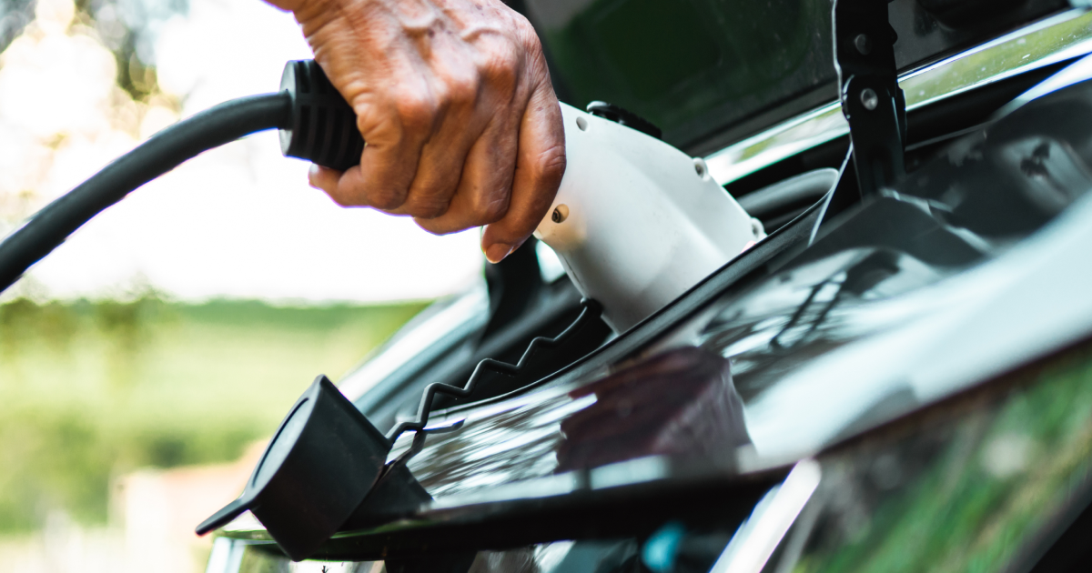 Hand plugging a charging cable into the charging port of an electric car.